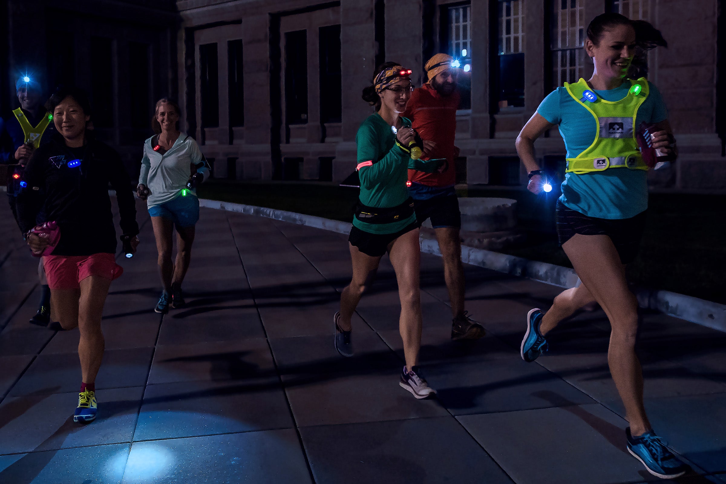 Group of runners wearing headlamps and lit vests running at night in urban setting