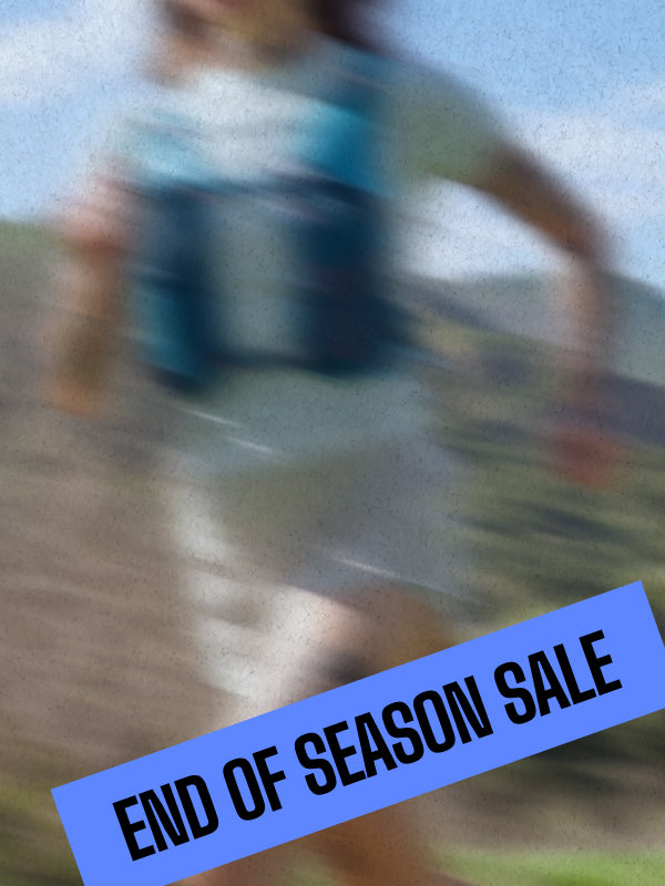 Three trail runners are seen from behind running on a dirt path through tall grass, wearing NATHAN hydration packs and athletic clothing.